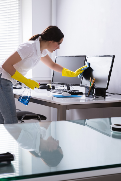 Professionelle Reinigungskraft der Schlueter Group bei der sorgfältigen Büroreinigung eines Arbeitsplatzes mit Computern in München.